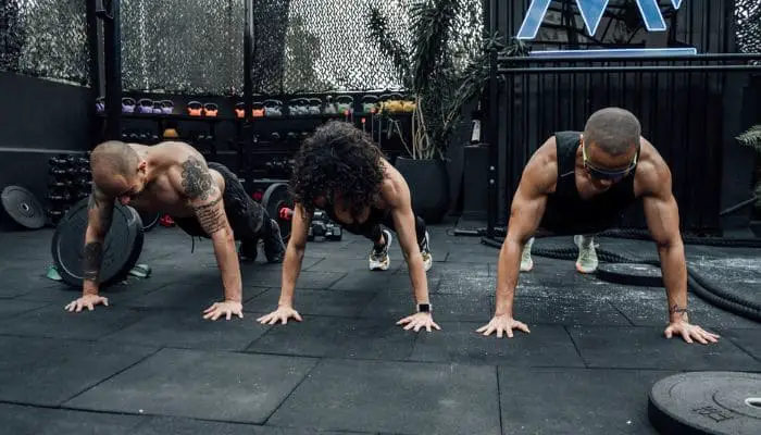 Dois homens e uma mulher realizando exercício de prancha em uma academia de crossfit