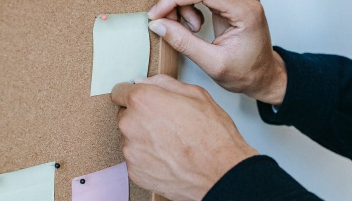 Mãos pregando papelzinho para lembrete em um quadro