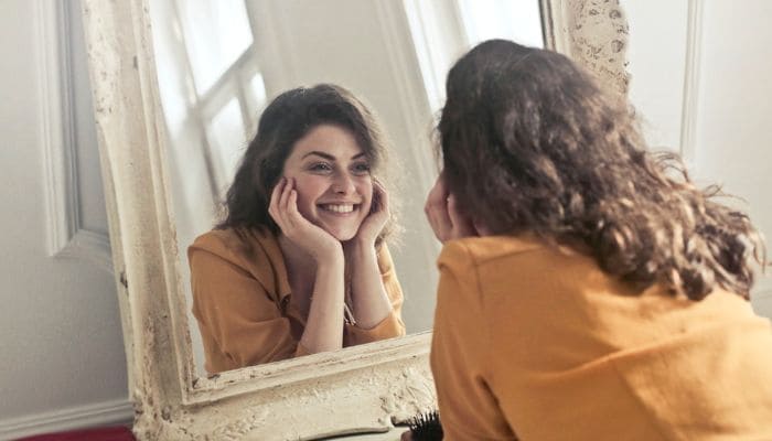 Garota com largo sorriso olhando-se no espelho