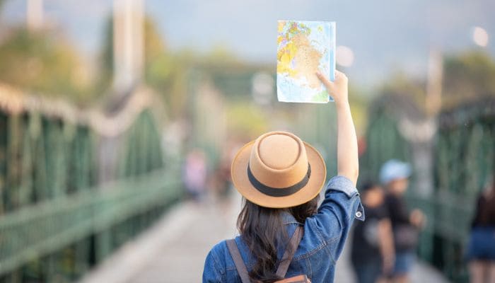 Mulher de chapéu observando mapa em ponto turístico