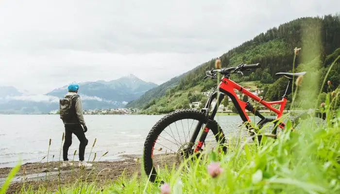 Homem com sua bicicleta vermelha em frente ao mar numa costa montanhosa