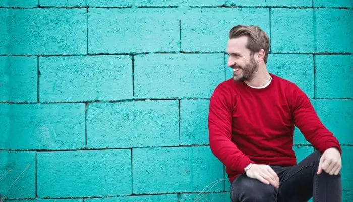 Homem sorrindo sentado de costas para um muro verde