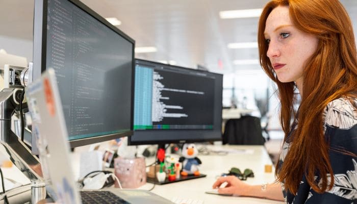 Bela mulher ruiva trabalhando com dois monitores de computador