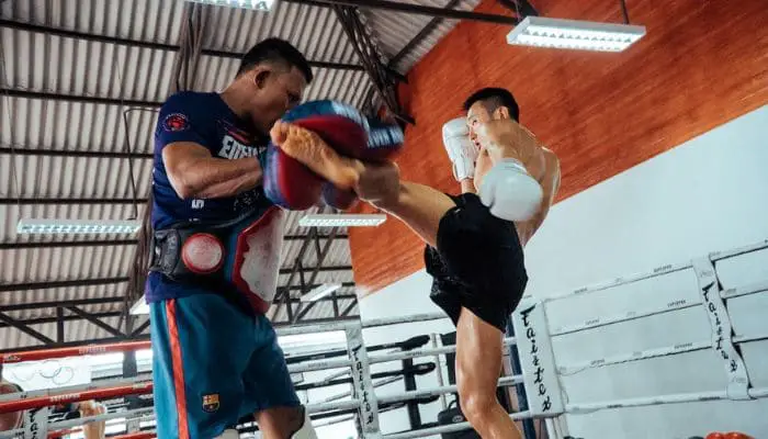 Homem treinando chute de Muay Thai em um ring com seu instrutor