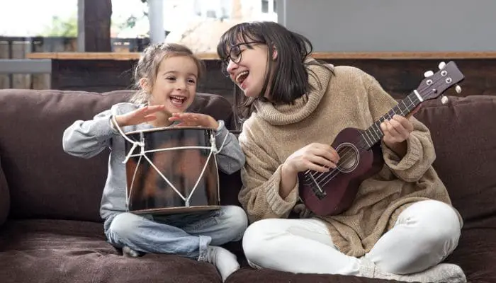 Mulher e sua filha felizes cantando e tocando cavaquinho e tambor sentadas no sofá