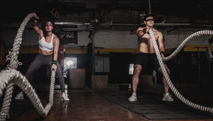 Homem e mulher praticando crossfit com corda naval