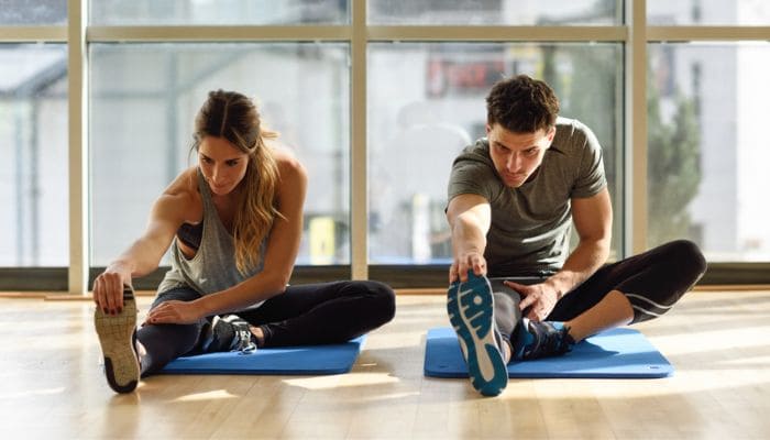 Homem e mulher se alongando sentados no chão sobre colchonetes de treino