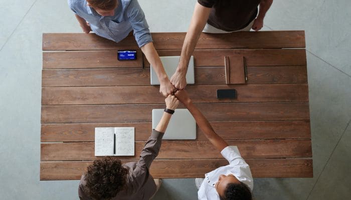 Quatro pessoas tocam os punhos cerrados sobre uma mesa