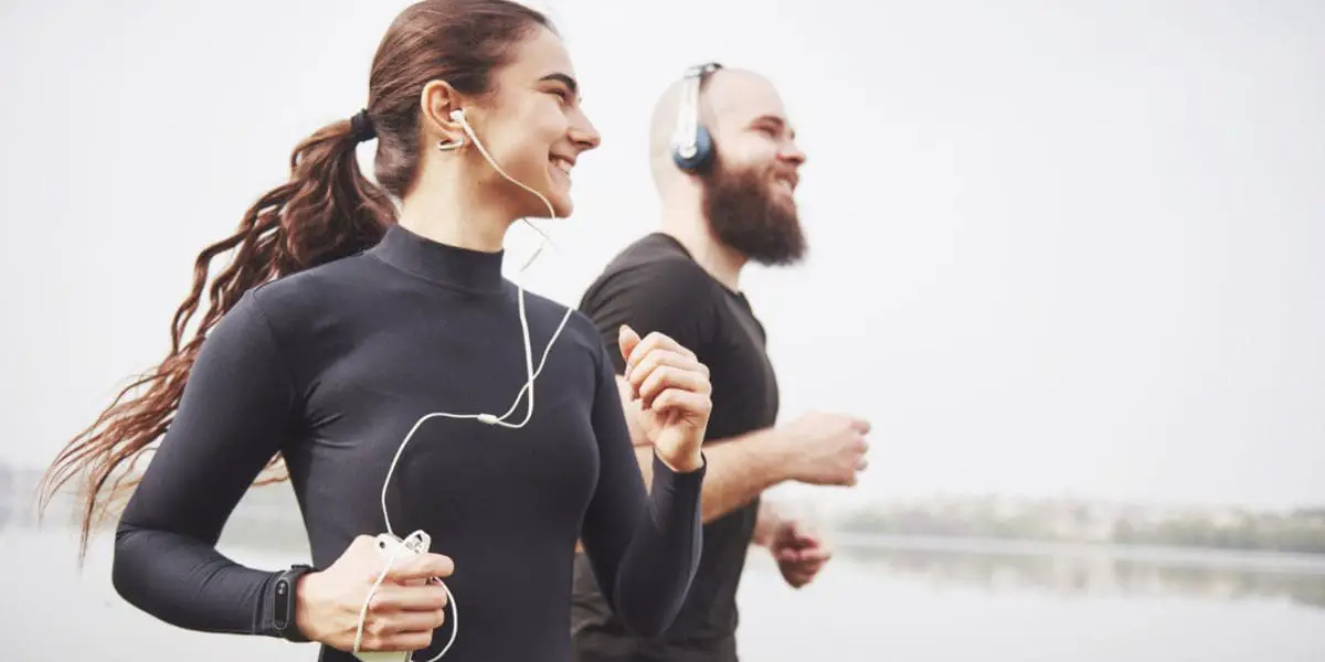 Casal sorridente praticando corrida para cuidar do bem-estar físico.