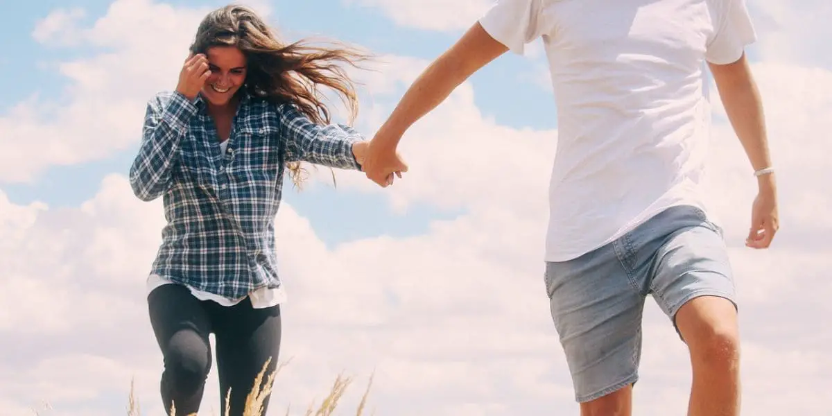 Casal sorridente realizando caminhada de mãos dadas.