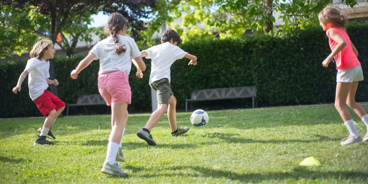 Esportes em Grupo: Crianças jogando futebol na grama.