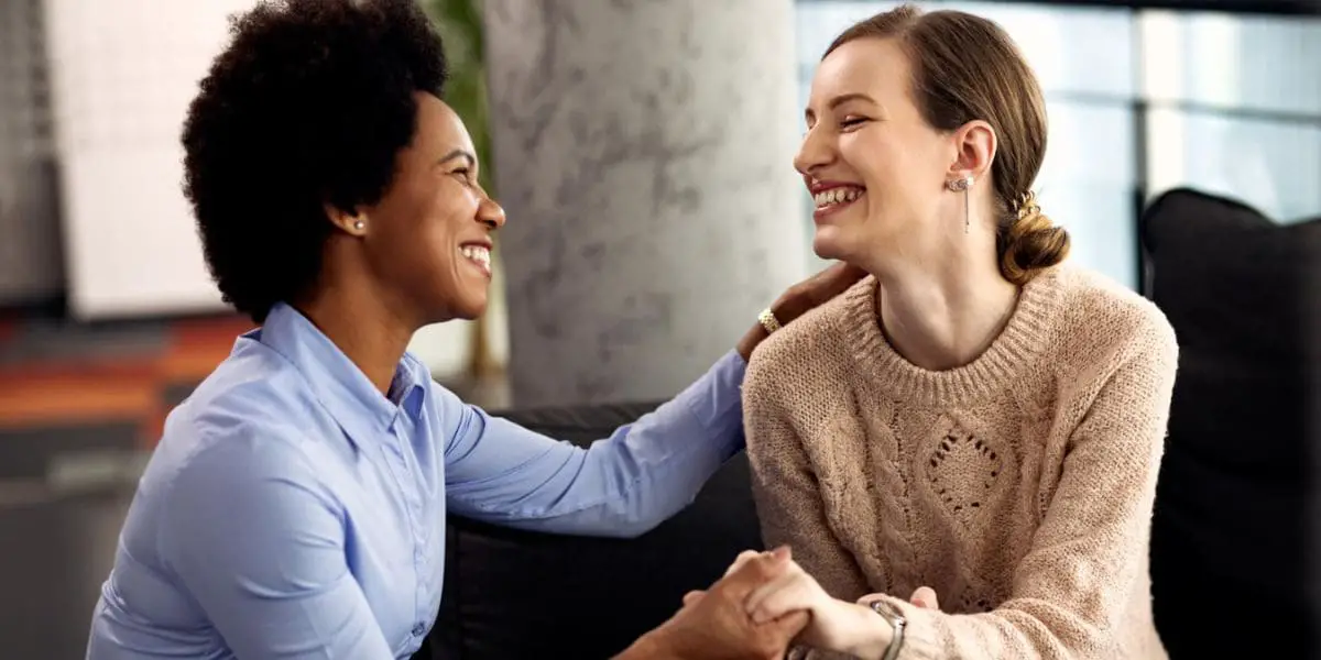 Duas amigas sorrindo de mãos dadas demonstrando empatia uma pela outra.