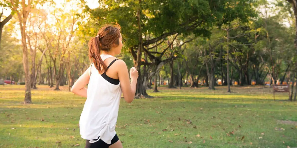 Exercícios Físicos: Garota praticando corrida em um parque.