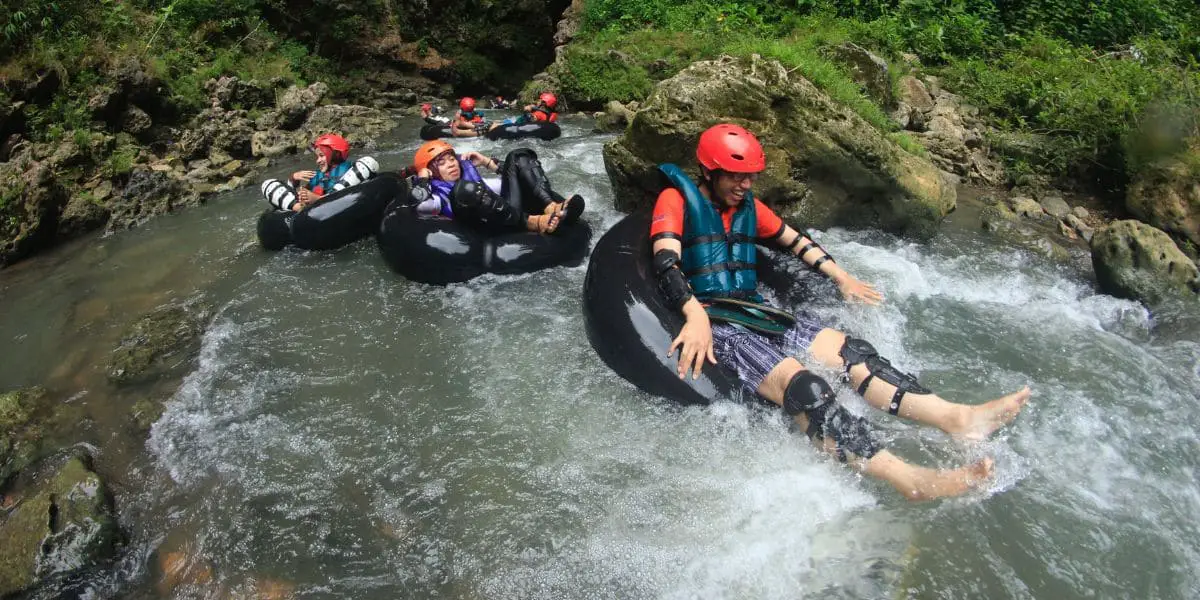 Esportes aquáticos: Grupo de pessoas sorridentes descendo correnteza de rio usando boias e equipamentos de proteção