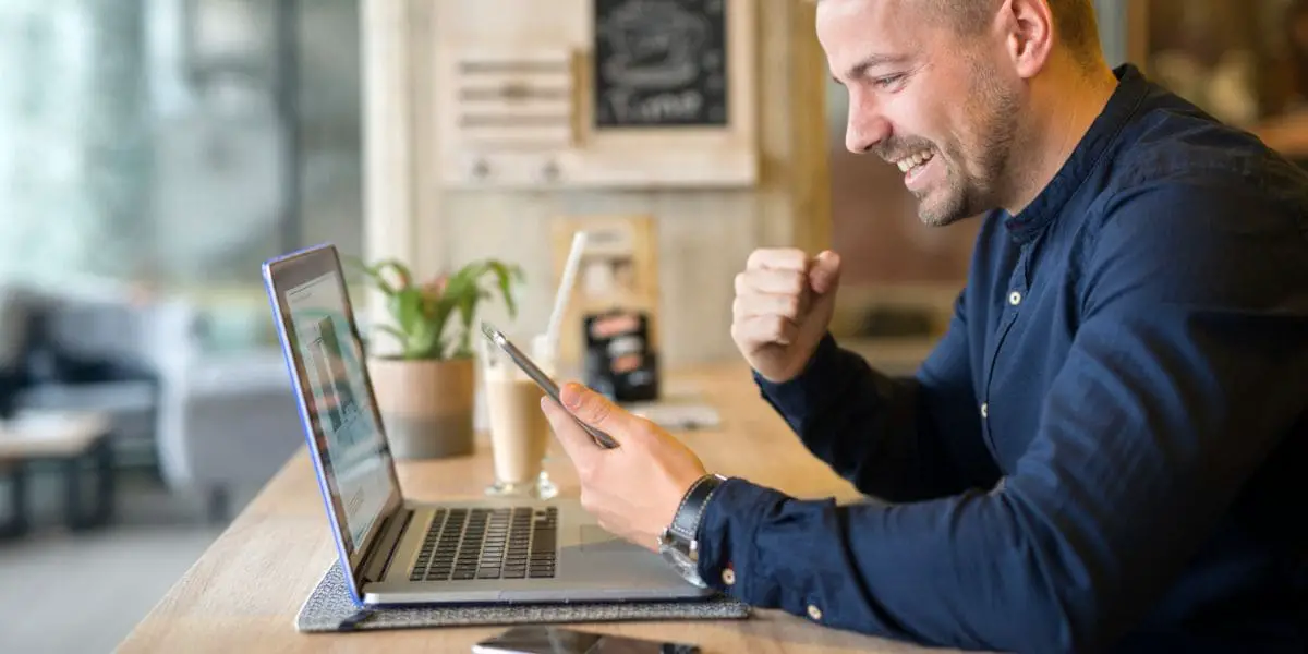 Homem comemorando ao ver uma mensagem no celular em seu empreendimento.