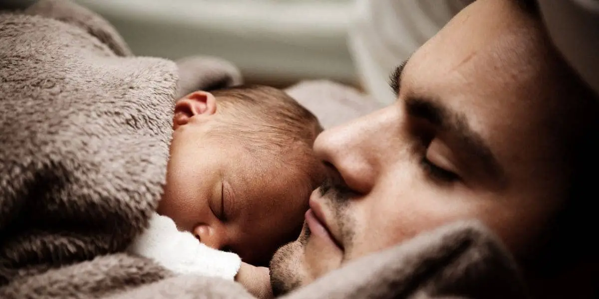 Dormir faz bem: Homem dormindo com um bebê em seu peito.