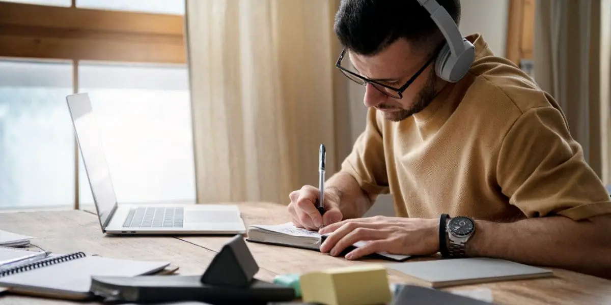 Como Aprender um Novo Idioma: Homem fazendo anotações de seus estudos usando fones de ouvido