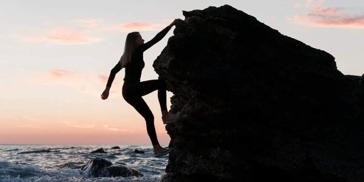 A Arte de Enfrentar Desafios: Mulher audaciosa escalando um rochedo em frente ao mar