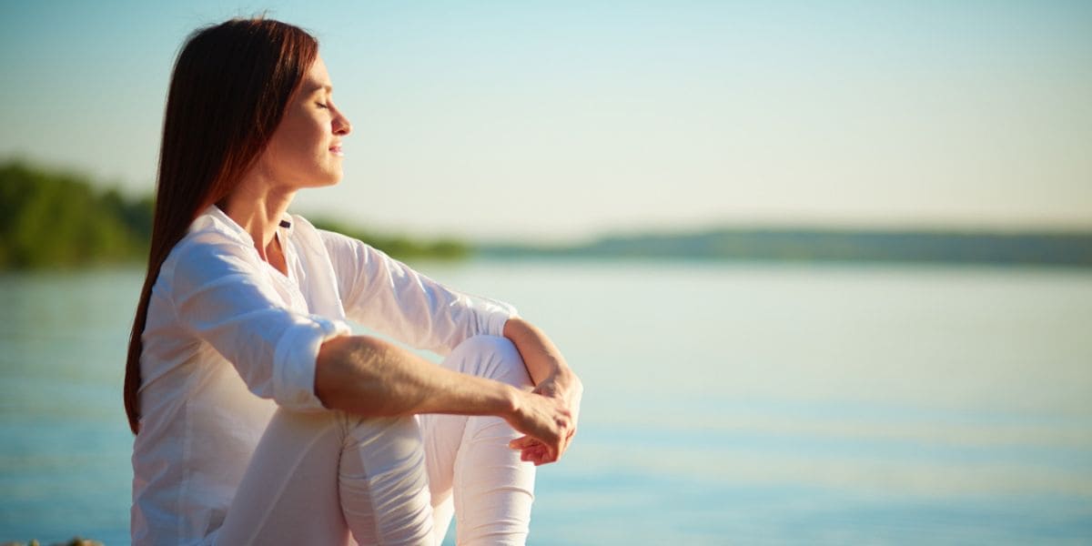 Atividade Física: Mulher com semblante calmo e feliz sentada perto de um lago.