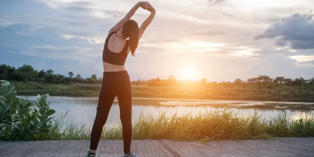 Tipos de exercícios físicos - mulher fazendo alongamento ao pôr do sol.