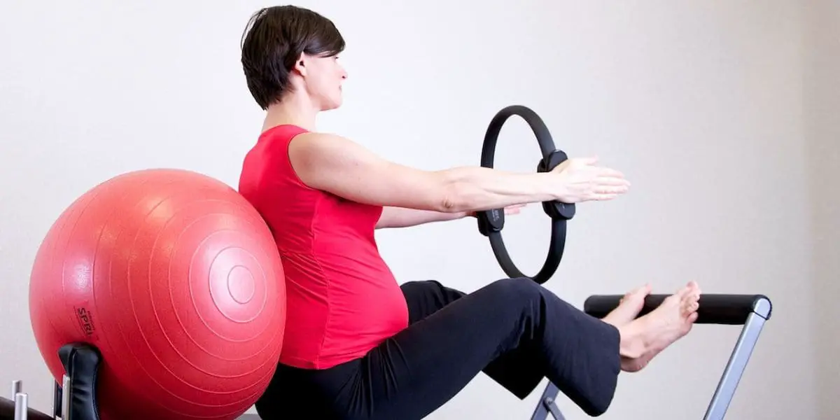 Mulher grávida praticando pilates com auxílio de aparelhos de ginástica.