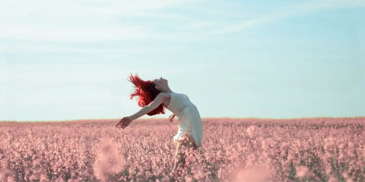 O Poder da Ação: Mulher com os cabelos vermelhos de braços abertos em um campo repleto de flores