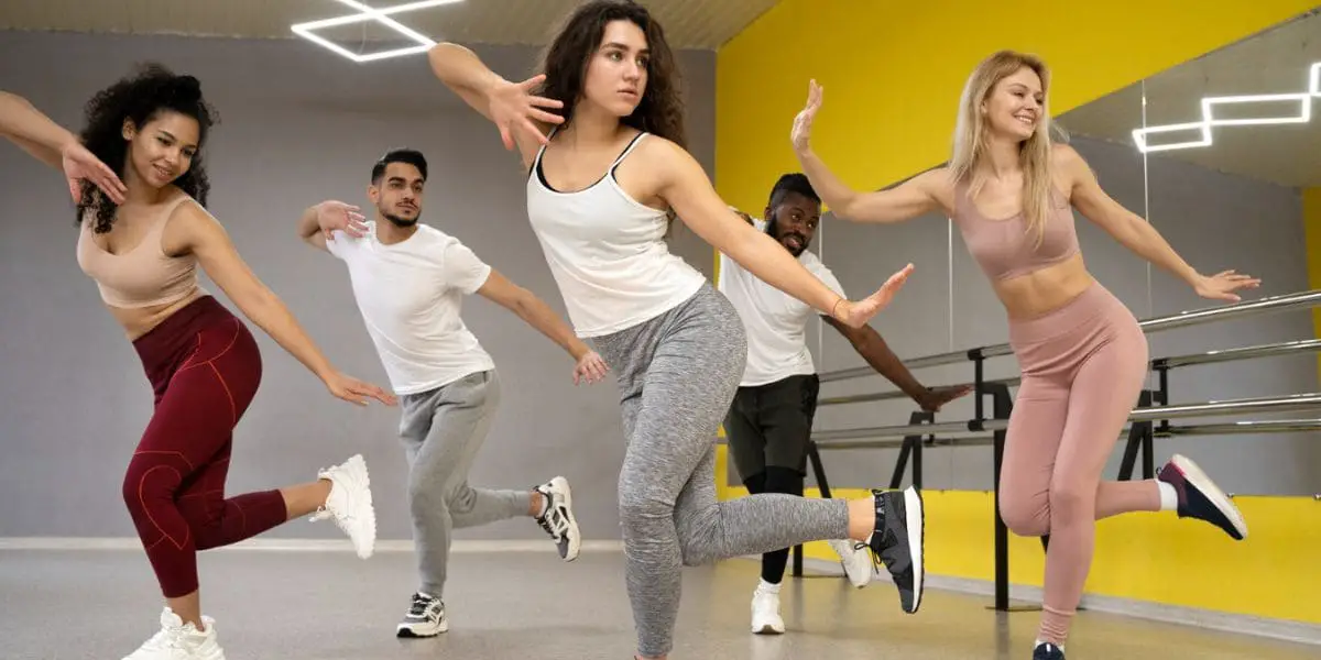 Pessoas com roupas de treino dançando zumba em um salão.