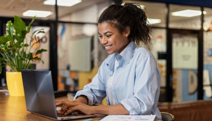 vista de perfil mulher sorrindo trabalhando com notebook no escritório